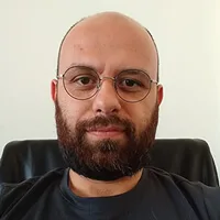 A bald man with glasses and a beard looks forward.