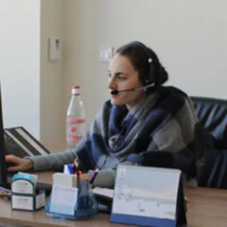 A woman wearing a headset works at her office desk in front of a computer.