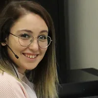 A young woman wearing glasses and a headset microphone smiles at the camera.