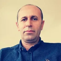 A portrait of a middle-aged man with short hair wearing a blue shirt and maintaining a neutral expression.
