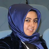 Portrait of a smiling woman wearing a blue headscarf and a dark blue velvet jacket.