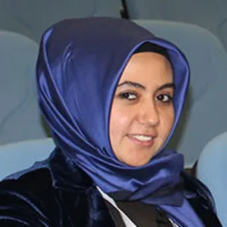 Portrait of a smiling woman wearing a blue headscarf and a dark blue velvet jacket.