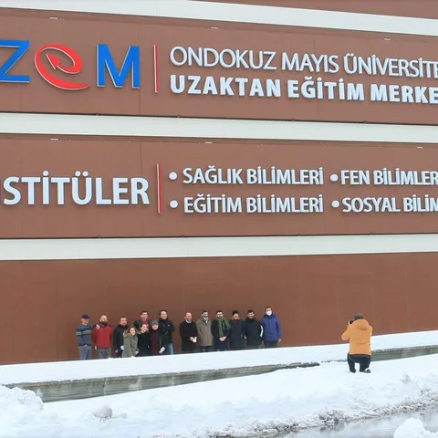 Ondokuz Mayıs Üniversitesi Uzaktan Eğitim Merkezi binasının girişinde karlı bir günde duran bir grup insan ve binadaki tabelalar görünmektedir.