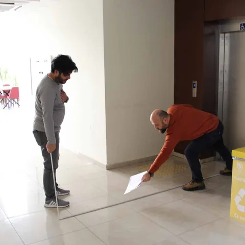 Erişilebilirlik çalışmasında beyaz bastonla koridorda ilerleyen katılımcı.