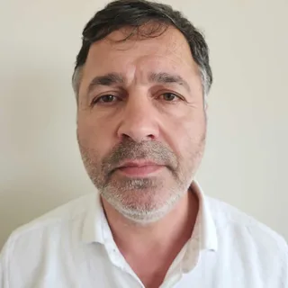 Portrait of Sebahattin against a plain background, wearing a white collared shirt.