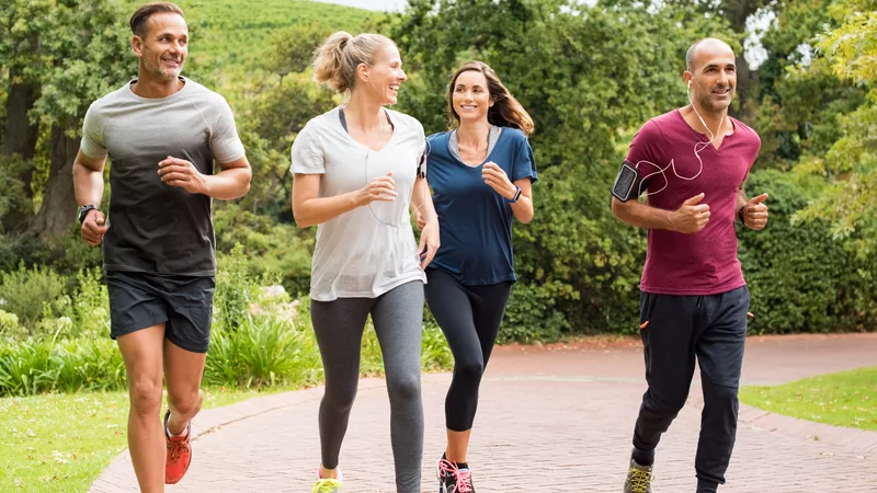 Parkta neşeyle koşan ve spor giyinen dört yetişkin.