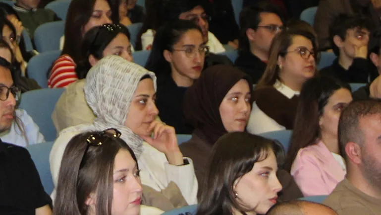 Konferans salonunda sıraları doldurmuş dinleyici topluluğu.