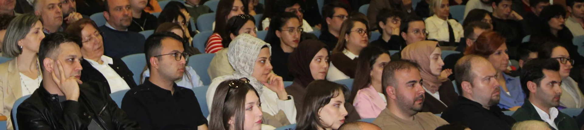 Konferans salonunda sıraları doldurmuş dinleyici topluluğu.