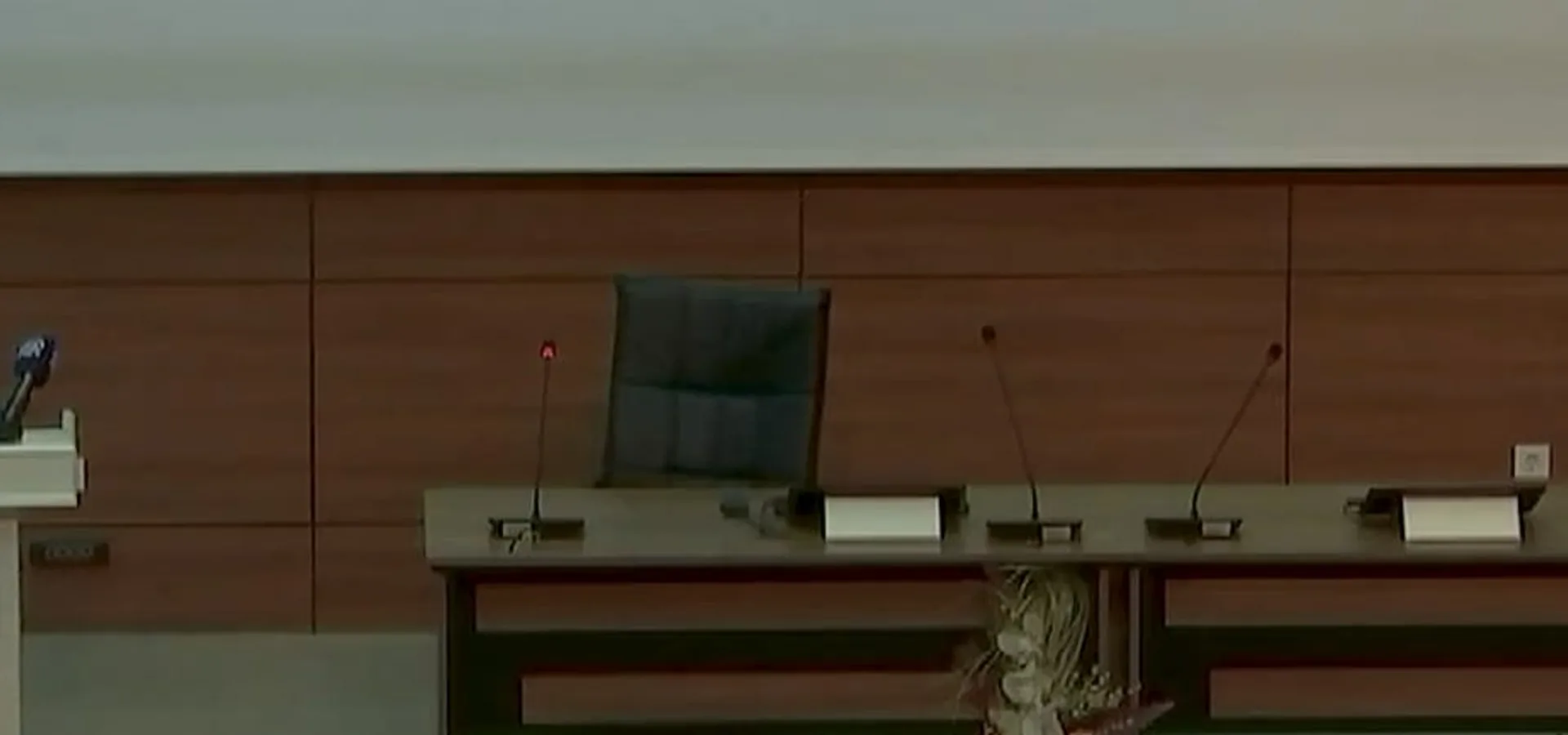 Konferans salonunda kürsüde konuşan bir kişi ve yanındaki boş panel masası.
