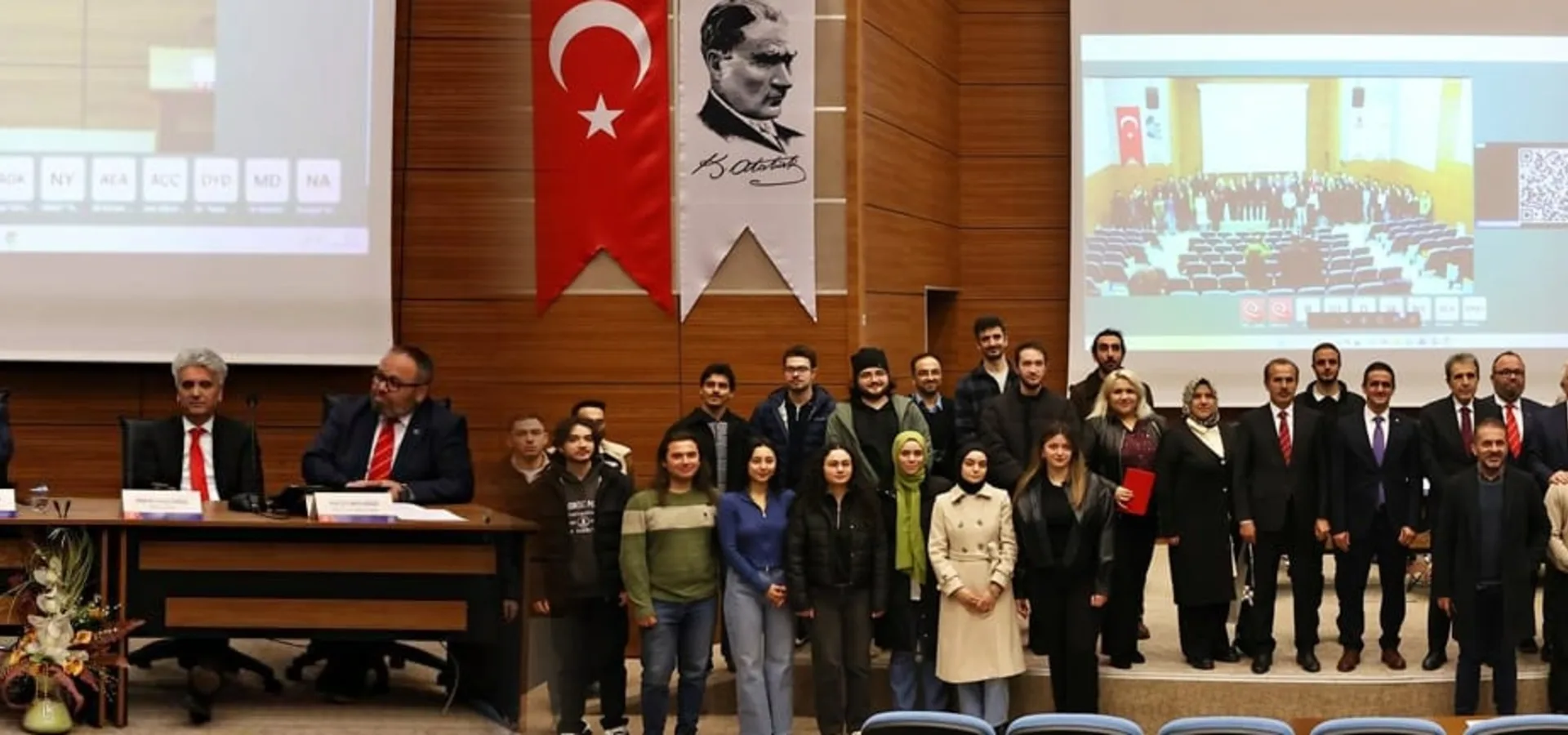 A group photograph in the hall at the end of a panel, with a Turkish flag, a portrait of Atatürk and the UZEM sign behind.