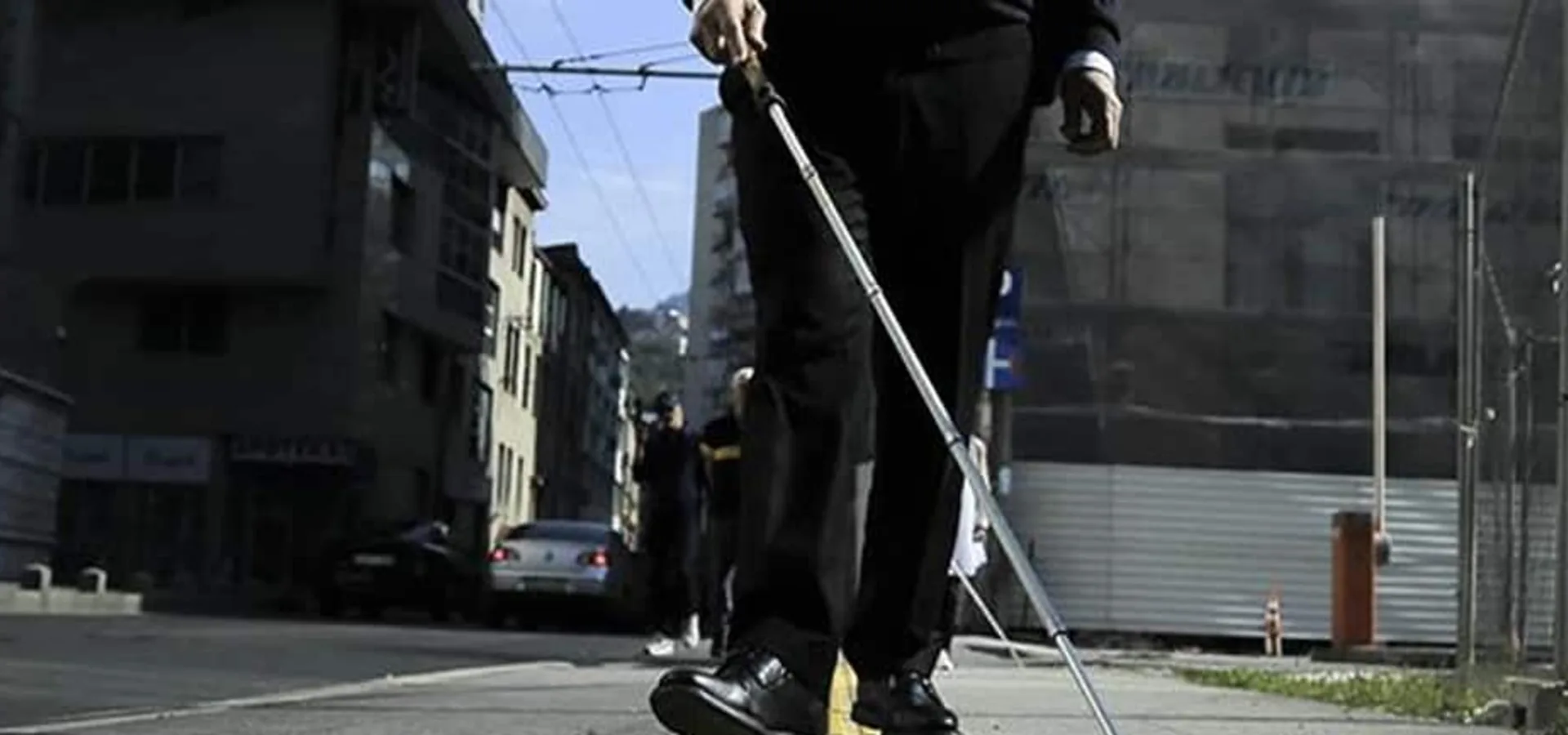 A person walking along a pavement using a white cane.