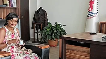 Two guests in armchairs in an office with their host at the head of the desk.