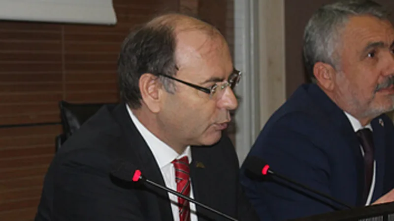 Panel masasında yan yana oturan üç yönetici; ortadaki mikrofona konuşuyor.