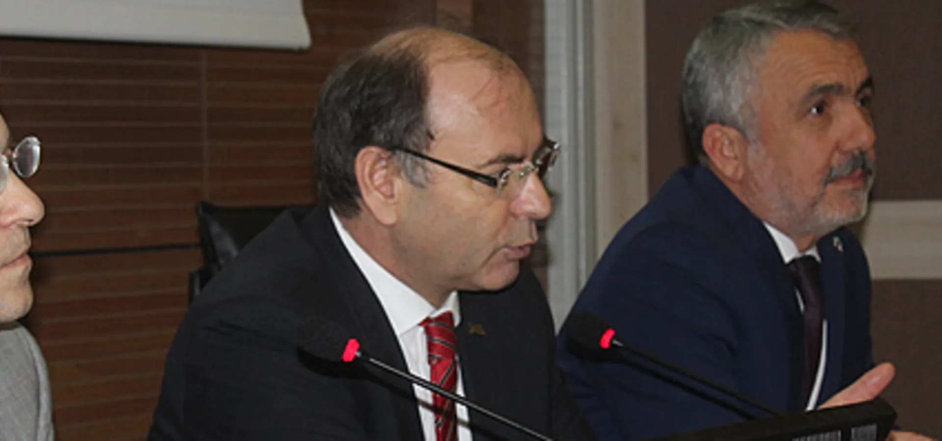 Panel masasında yan yana oturan üç yönetici; ortadaki mikrofona konuşuyor.