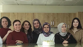 A group photograph of ten women members of staff standing behind a kitchen counter with a small cake on it.